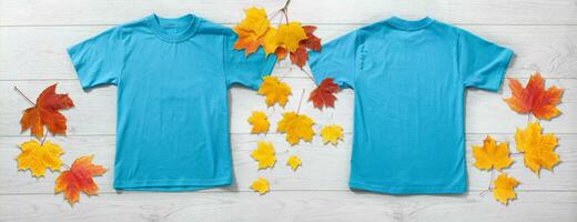 Front and back views on boys t-shirts on white wooden desk background with autumn lievs. Mockup for design closeup photo