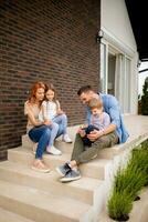 Family with a mother, father, son and daughter sitting outside on the steps of a front porch of a brick house photo