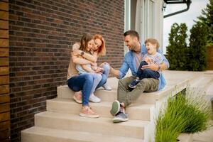 Family with a mother, father, son and daughter sitting outside on the steps of a front porch of a brick house photo