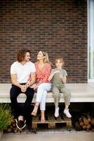 Family with a mother, father and daughter sitting outside on the steps of a front porch of a brick house photo