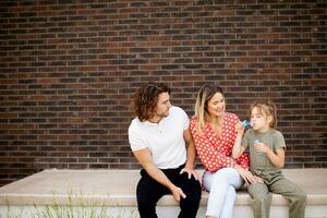 Family with a mother, father and daughter sitting outside on the steps of a front porch of a brick house photo