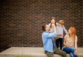 Family with a mother, father, son and daughter sitting outside on steps of a front porch of a brick house and eating strawberries photo