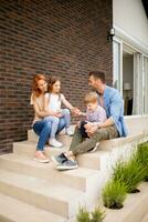 Family with a mother, father, son and daughter sitting outside on the steps of a front porch of a brick house photo