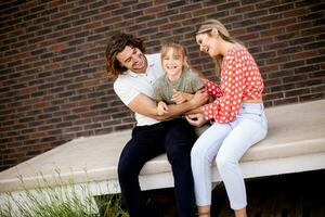 Family with a mother, father and daughter sitting outside on the steps of a front porch of a brick house photo