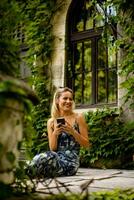 Pretty young woman using mobile phone by the old house with ivy photo