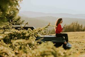 mujer joven relajándose en el capó de un vehículo de terreno en el campo foto