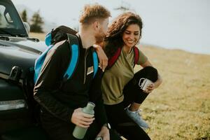 pareja joven relajándose en el capó de un vehículo todoterreno en el campo foto