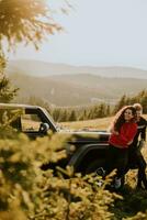 pareja joven relajándose en el capó de un vehículo todoterreno en el campo foto