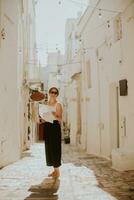 hembra turista con papel ciudad mapa en estrecho calles de ostuni, Italia foto