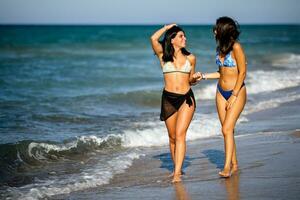 dos bonito joven mujer teniendo divertido en el playa foto