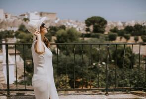 A young woman in a white dress with white hat during tourist visit in Alberobello, Italy photo