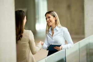 Two young business women with paper notebook in the office hallway photo