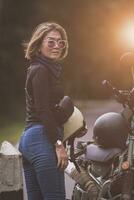 pretty woman holding safety helmet standing on local road beside small enduro motorcycle photo