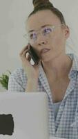 a woman in glasses talking on the phone while using a laptop video