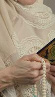une femme dans une blanc hijab prier en utilisant prière perles et une livre video