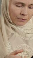 un mujer en un blanco hijab Orando utilizando oración rosario y un libro video