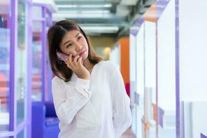 hermosa asiático negocio mujer es en pie y hablando en el teléfono con un pasivo expresión mientras mirando a el Copiar espacio y comunicado con su clientes, digital marketing. foto