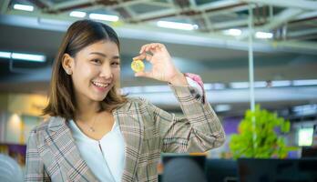 Beautiful asian business woman holding bitcoin while looking to photo