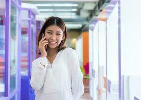 hermosa asiático negocio mujer es en pie y hablando en el teléfono con un contento sonrisa, digital marketing. foto