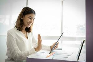 Beautiful asian businesswoman greeting customers via tablet with professional smile. photo