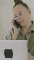 a woman in glasses talking on the phone while using a laptop video