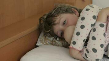 uma pequeno menina deitado dentro cama com uma boneca video