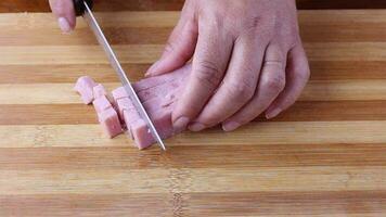 Female hand slicing raw ham cubes on cutting board video