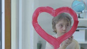 un niño pintura un corazón forma rojo línea en frente de un ventana video