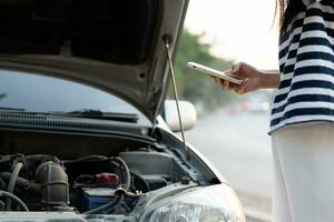 breakdown, broken car, repair. Woman uses mobile phone check insurance premiums through application due to car accident . Find garage to get car fixed during country tour, waiting for help, emergency. photo