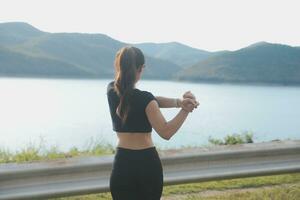 joven hermosa asiático mujer en Deportes trajes haciendo extensión antes de rutina de ejercicio al aire libre en el parque en el Mañana a obtener un sano estilo de vida. sano joven mujer calentamiento arriba al aire libre. foto