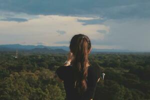 Young woman traveler in casual clothes with backpack from back on background of beautiful view on mountains photo