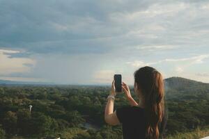 Young woman traveler in casual clothes with backpack from back on background of beautiful view on mountains photo