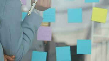 Young asian business woman working on project plan using sticky papers notes on glass wall, people meeting to share idea, Business design planning concepts. video