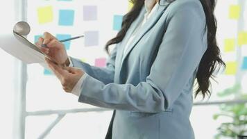 Young asian business woman working on project plan using sticky papers notes on glass wall, people meeting to share idea, Business design planning concepts. video