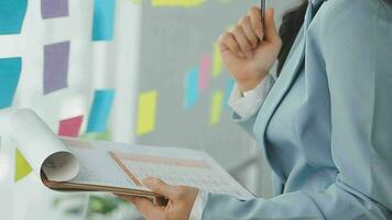 Young asian business woman working on project plan using sticky papers notes on glass wall, people meeting to share idea, Business design planning concepts. video