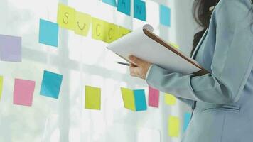 Young asian business woman working on project plan using sticky papers notes on glass wall, people meeting to share idea, Business design planning concepts. video