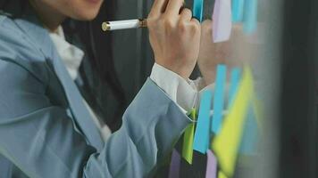 Young asian business woman working on project plan using sticky papers notes on glass wall, people meeting to share idea, Business design planning concepts. video