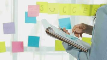 Young asian business woman working on project plan using sticky papers notes on glass wall, people meeting to share idea, Business design planning concepts. video