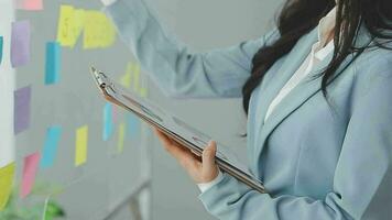 Young asian business woman working on project plan using sticky papers notes on glass wall, people meeting to share idea, Business design planning concepts. video