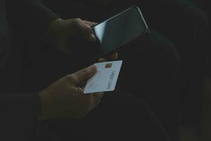 A credit card in the hands of a young businesswoman pays for a business on a mobile phone and on a desk with a laptop. photo