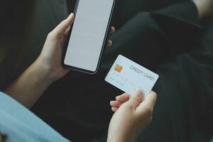 A credit card in the hands of a young businesswoman pays for a business on a mobile phone and on a desk with a laptop. photo