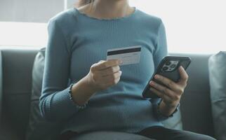 un crédito tarjeta en el manos de un joven mujer de negocios paga para un negocio en un móvil teléfono y en un escritorio con un ordenador portátil. foto