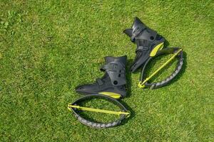 Kangoo jump boots on green grass. Black Kangoo sneakers with yellow turf patches. Modern shoes for fitness, aerobics. photo