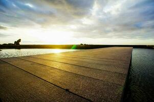 a wooden dock with the sun setting over it photo