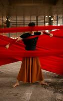 an Asian man standing proudly among the red cloth that dangles in an old building photo