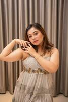 an Asian woman wearing a gray dress and beautiful makeup while standing in front of luxurious curtains at a party photo