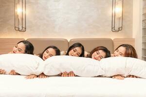 a group of Asian women are sleeping and leaning on white pillows with their friends in a luxury hotel photo