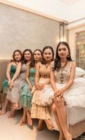a group of Asian women sitting together on a white bed while wearing dresses and makeup during a party at a friend's house photo