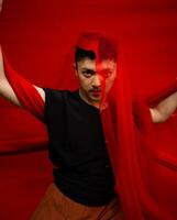an Asian man standing in front of a red cloth with a red cloth hanging over his head photo