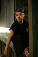 an Asian man hanging from the iron of an abandoned building while wearing a black shirt photo